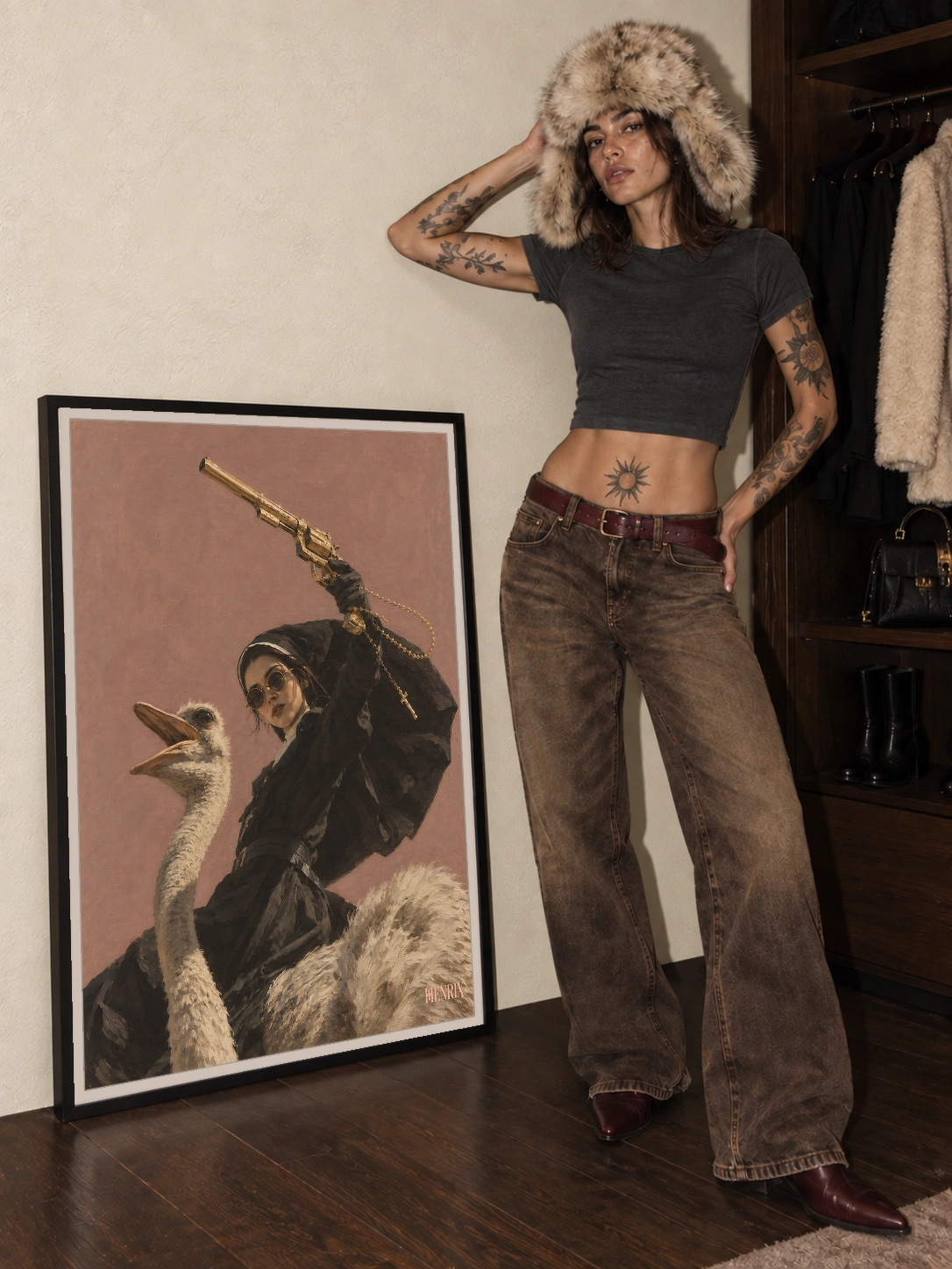 Divine Departure print, 36 × 48 inch, black frame leaning on the floor beside a tattooed woman wearing brown trousers and a fur hat