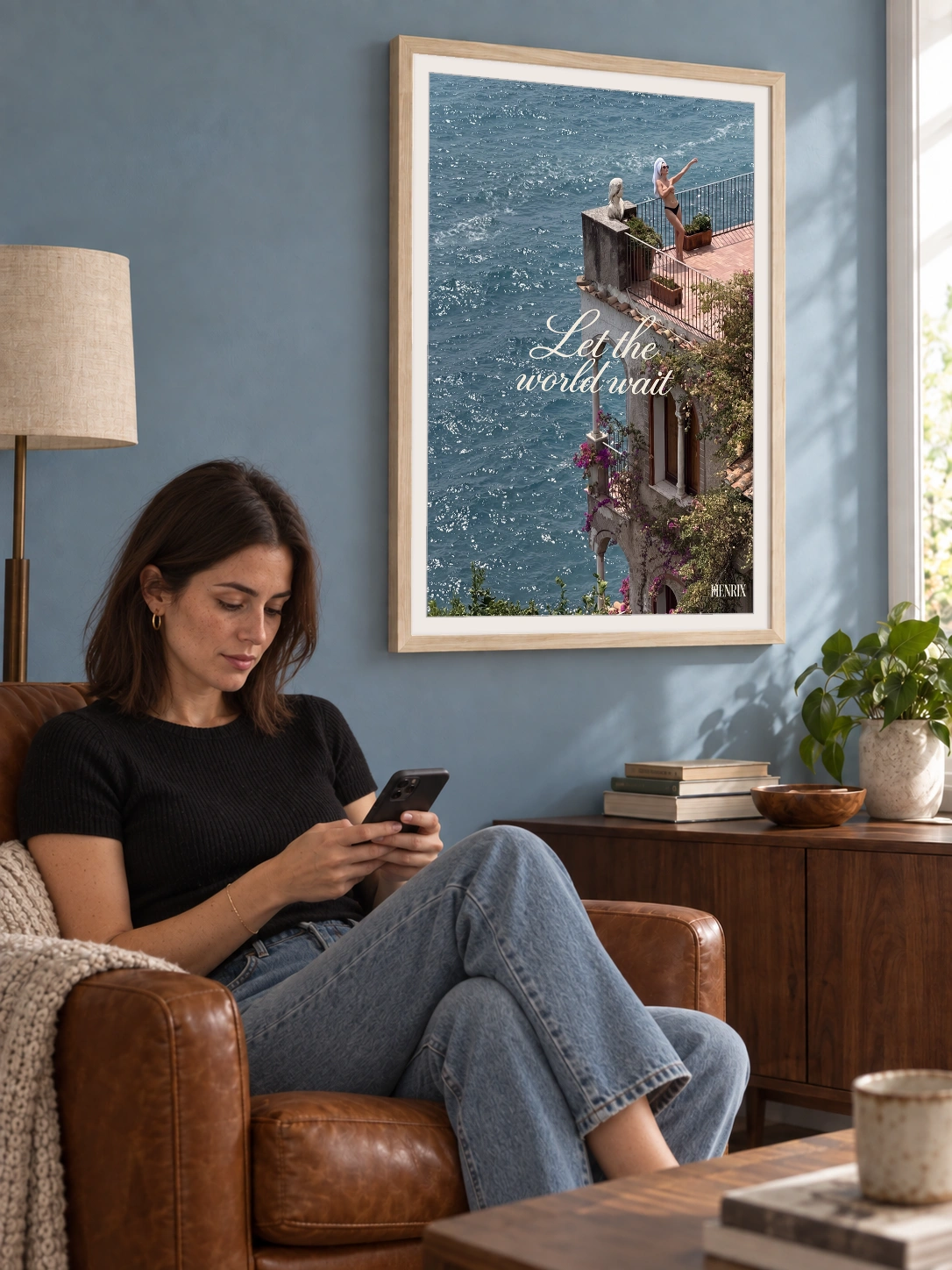 Let the World Wait print, 18 × 24 inch, Natural Wood frame above a seated woman checking her phone, viewed at an angle