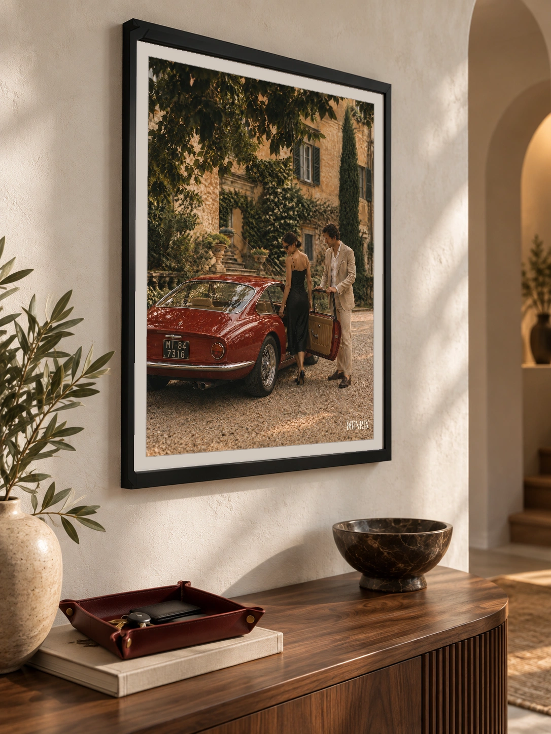 The Gentleman print, 18 × 24 inch, black frame above a wood console beside an arched doorway, viewed at an angle