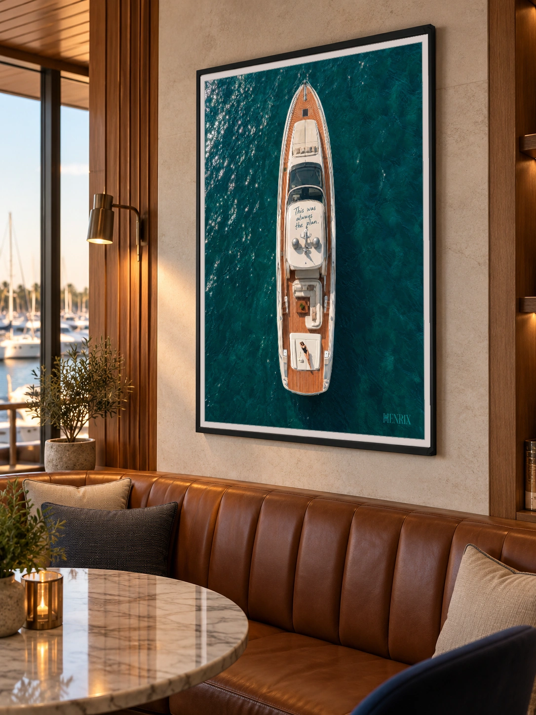This Was Always the Plan print, 36 × 48 inch, black frame above a leather banquette by a waterside window, viewed obliquely