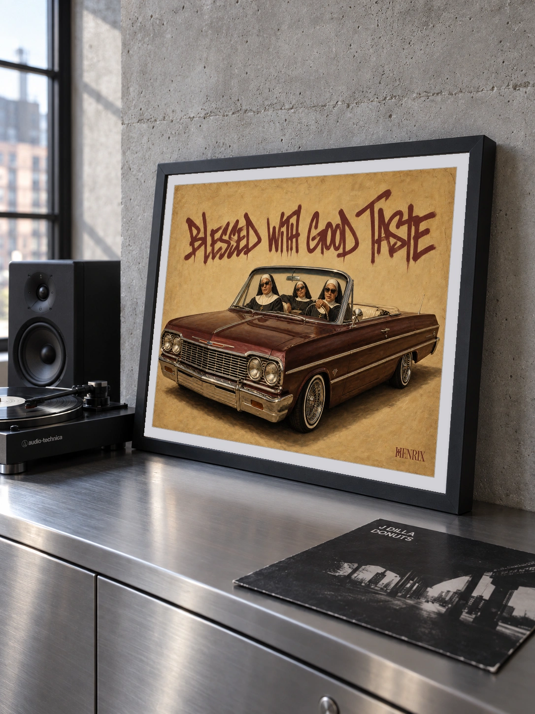 Blessed With Good Taste print, 24 × 18 inch, small black frame leaning on a metal console beside a speaker, viewed obliquely