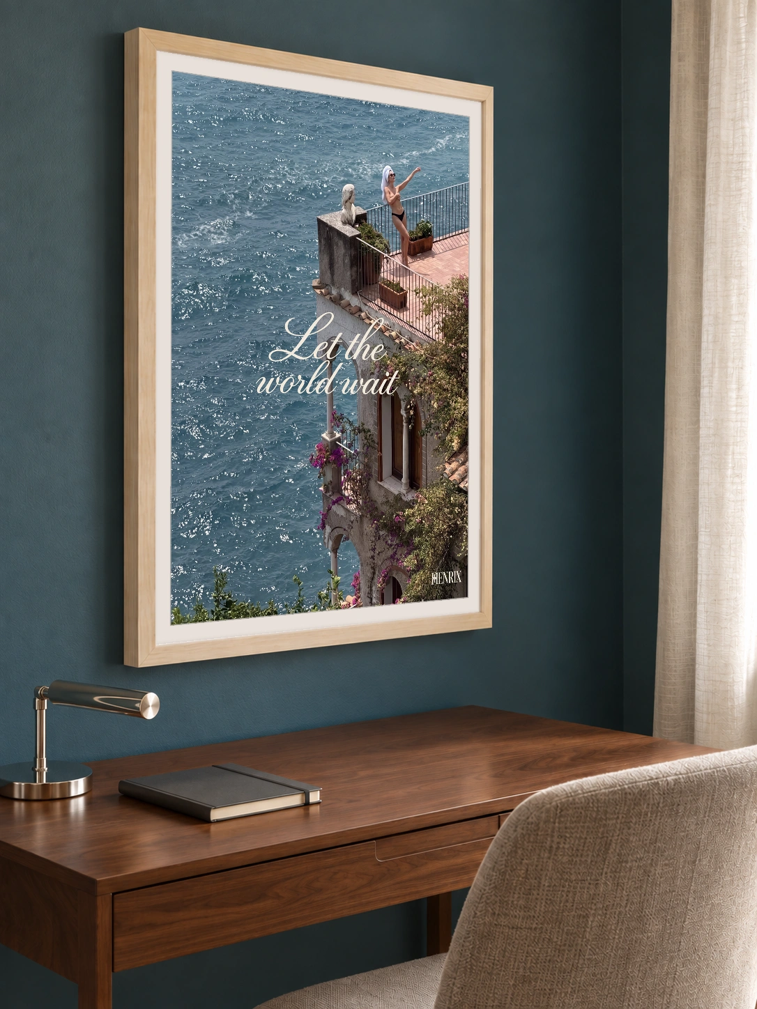 Let the World Wait print, 18 × 24 inch, Natural Wood frame above a wood desk on a dark teal wall, viewed obliquely